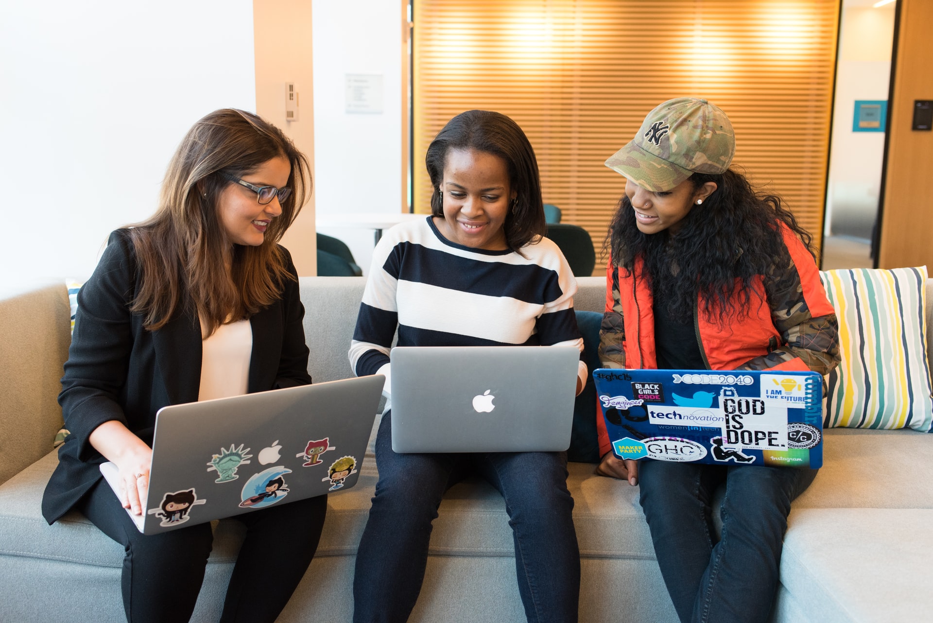 three women sitting on a couch and holding laptops