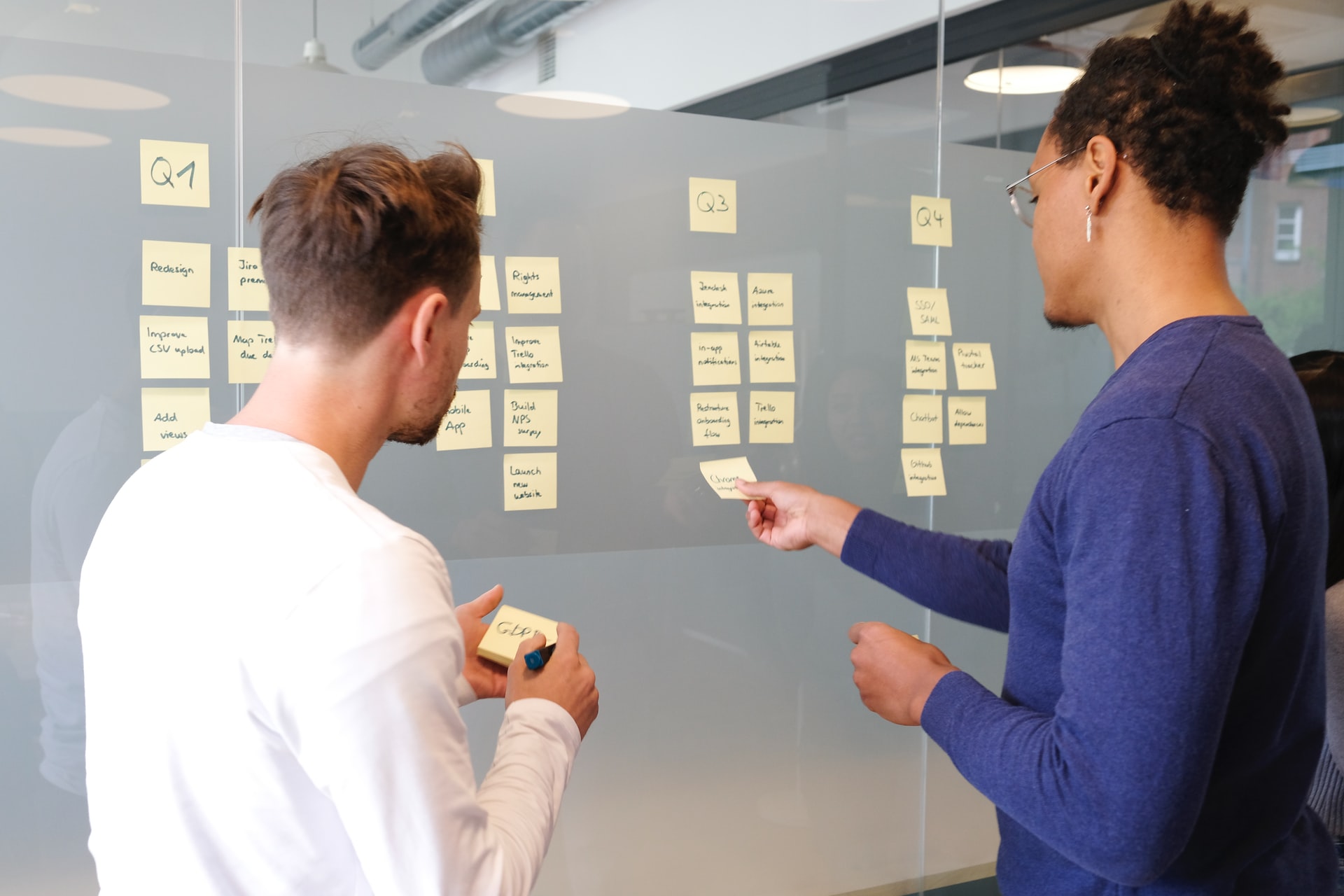 coworkers adding post it notes on a glass wall