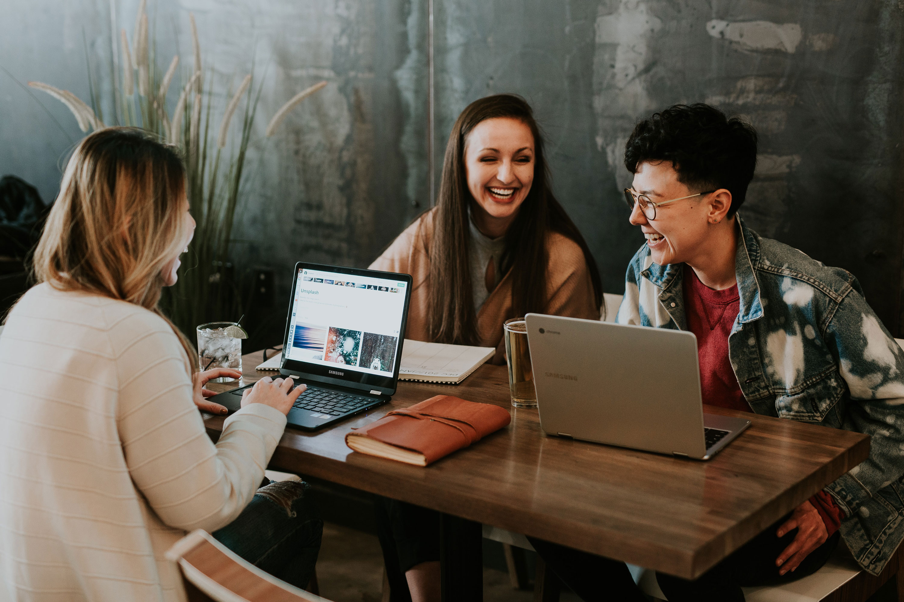 women sitting at table with laptops, laughing