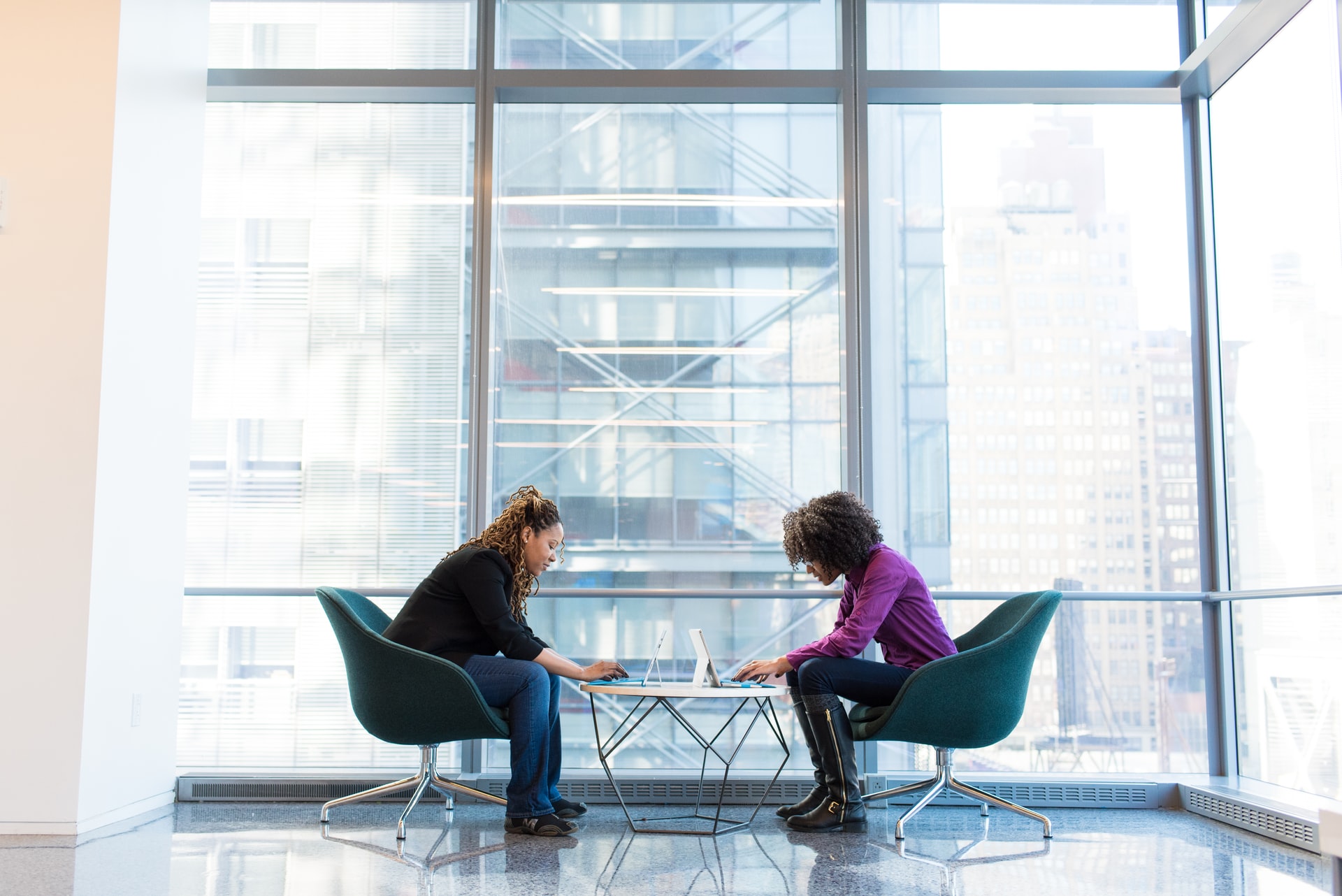two women working on laptops in a building with a glass wall