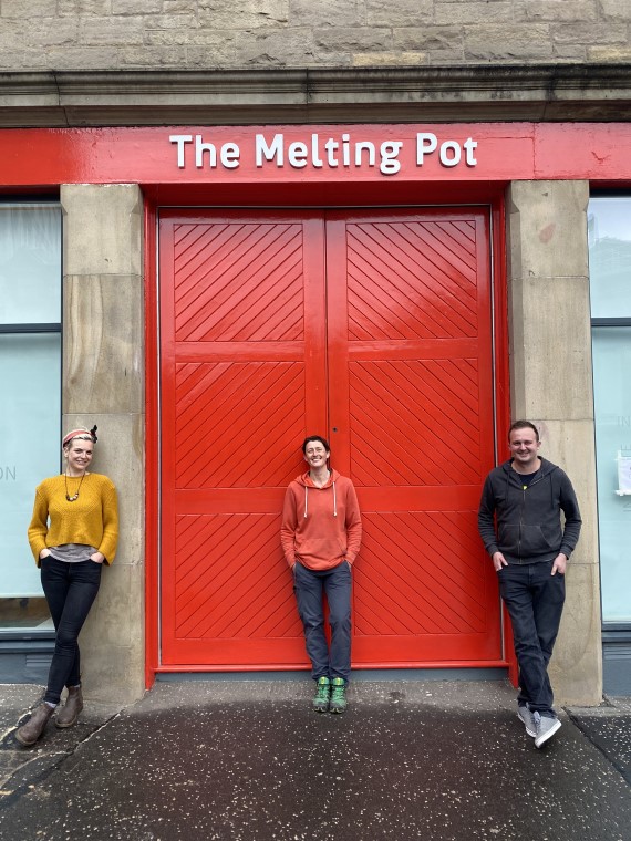 three persons standing in front of a red door of The Melting Pot