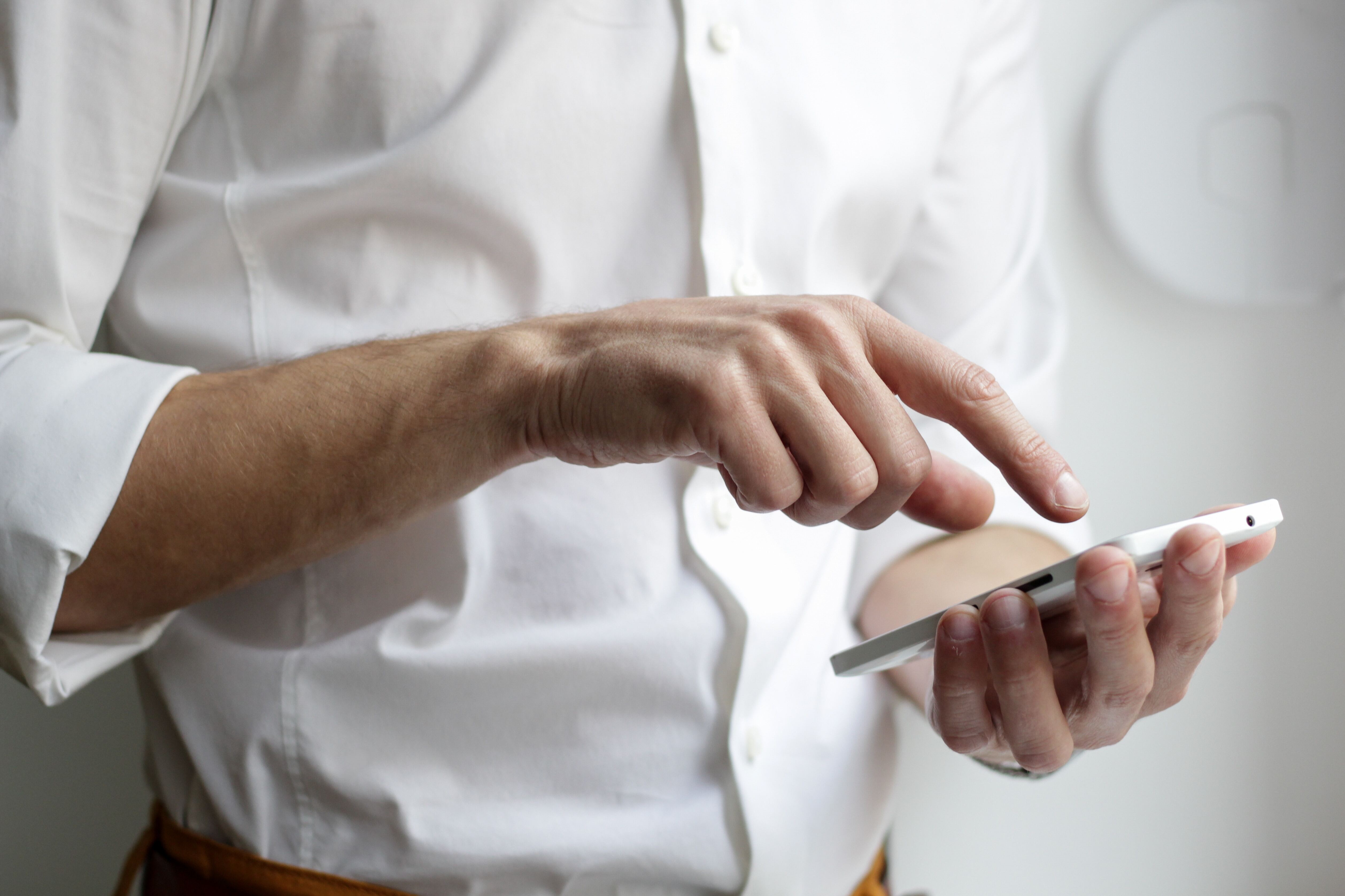 man in a white shirt typing on smartphone