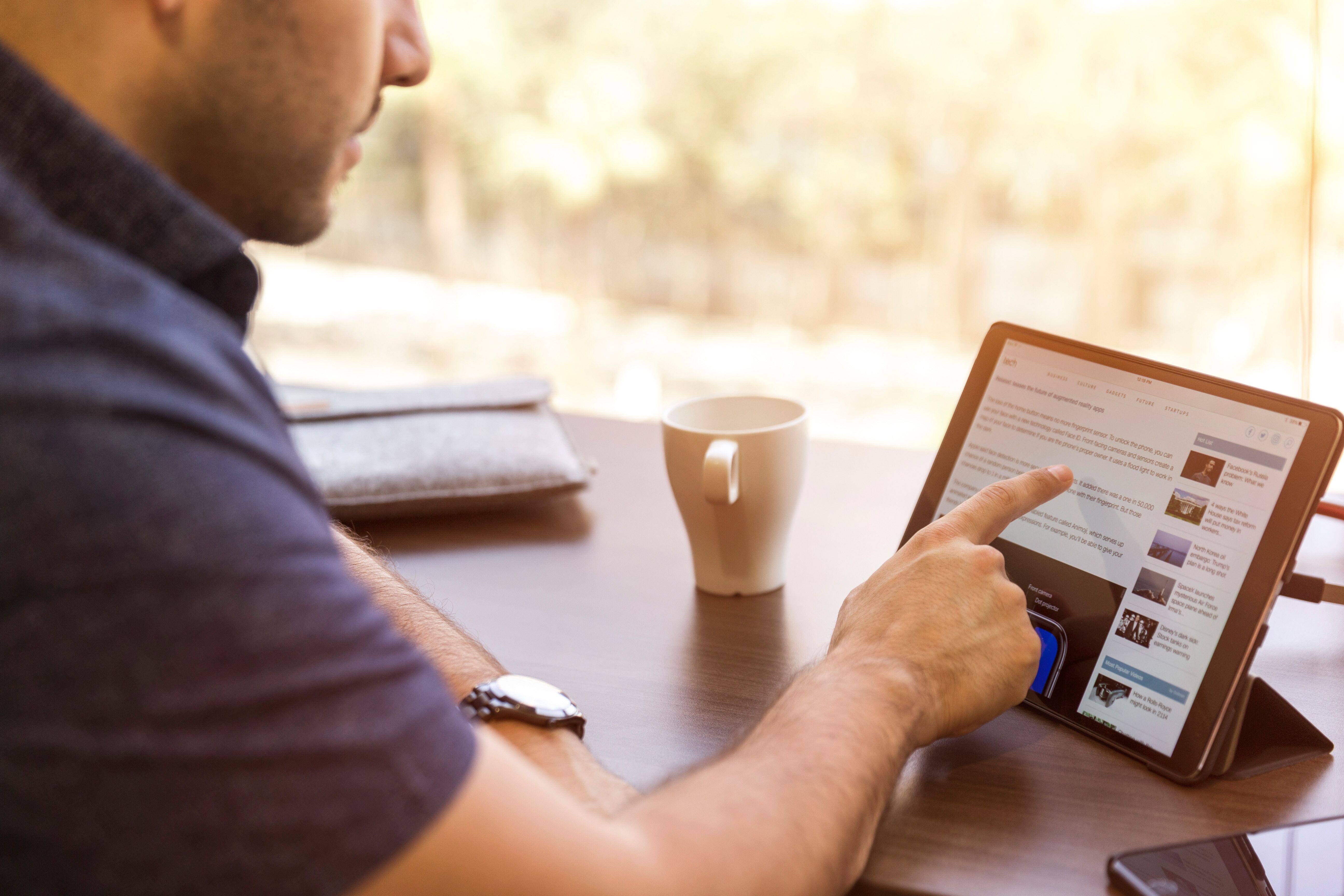 man drinking coffee and scrolling an article on a tablet