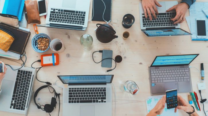 Lots of laptops and phones on a table with coffee mugs