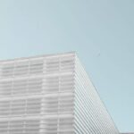 A photo of the top of a white modern office block against a pale blue sky