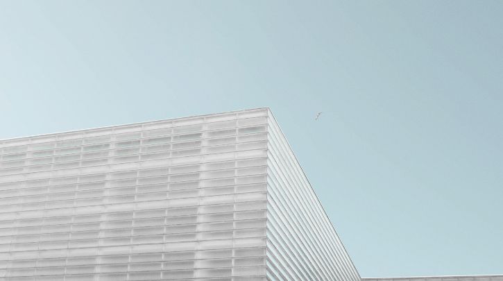A photo of the top of a white modern office block against a pale blue sky